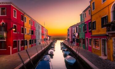 Vibrant facades along Burano's canal with boats at serene sunset. Perfect travel snapshot.