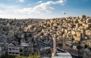 Aerial view of Amman's urban landscape with the Jordanian flag waving.