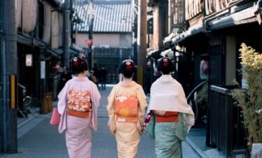 Three women wearing traditional kimonos walk down a historic street in Kyoto, Japan, capturing cultural essence.