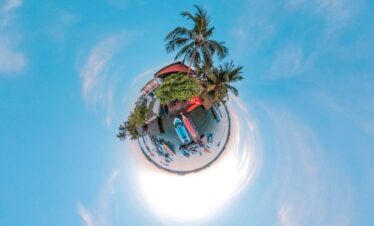 A creative tiny planet aerial view of a vibrant tropical beach scene surrounded by ocean, boats, and palm trees in Sri Lanka.